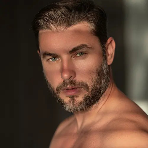 Oberkoerper_und_Gesicht_eines_jungen_Mannes_mit_Bart_der_dich_gerade_anblickt